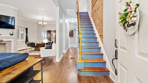 Un intérieur moderne avec un escalier en bois, un coin repas et un salon comprenant un canapé et un téléviseur.