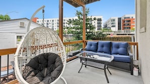 Un balcon avec un fauteuil suspendu blanc, un canapé bleu et une table en verre.
