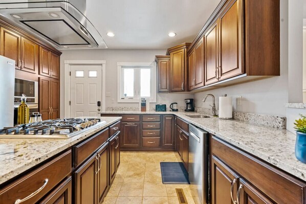 A modern kitchen with wooden cabinets, granite countertops, a gas stove, and a dishwasher.