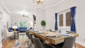 Un espace repas moderne avec une table en bois dressée pour quatre personnes, entourée de chaises grises. Un ventilateur de plafond et un lustre sont visibles au-dessus de la table.
