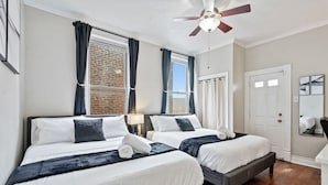 Une chambre d’hôtel avec deux lits, un ventilateur de plafond, un mur en briques et une porte.