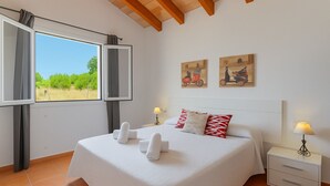 Une chambre à coucher avec un grand lit, deux tableaux accrochés au mur, une fenêtre avec des rideaux et une table de chevet avec une lampe.