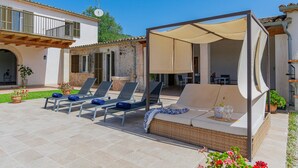 Une terrasse avec des chaises longues, un espace salon abrité et des plantes en pot.