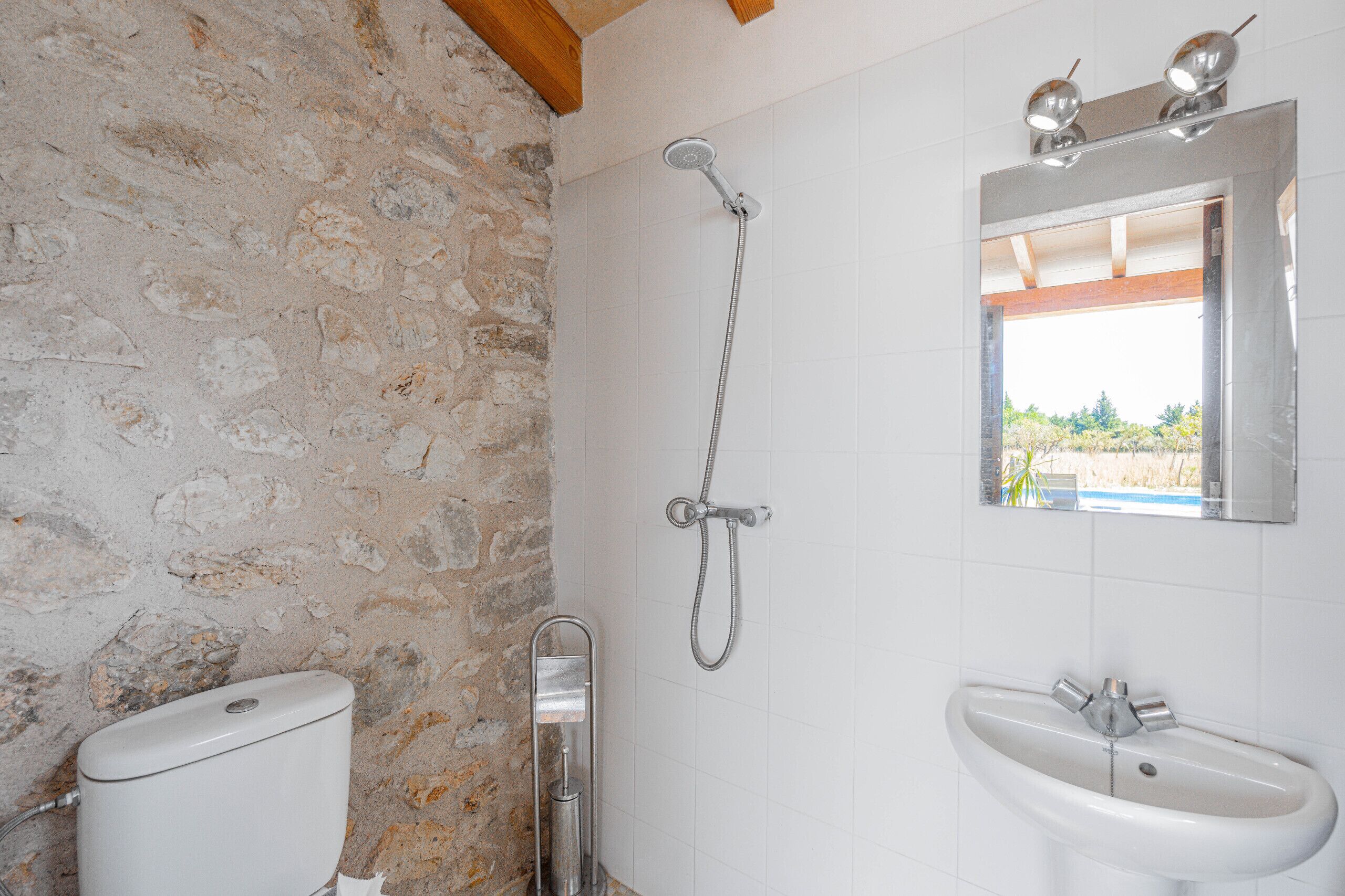 A bathroom with a stone wall, a shower, a toilet, and a sink.
