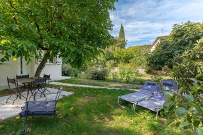 A patio with a table and chairs, a lounge chair, and a garden with various plants and a tree.