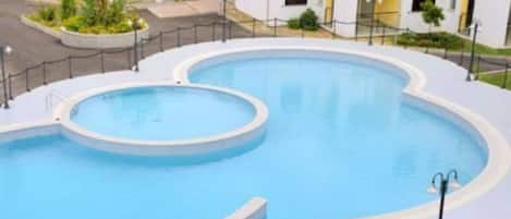 A large, circular swimming pool with a surrounding walkway and a fence.