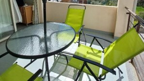 A balcony with a glass table and chairs, an umbrella, and a view of buildings in the background. - 1BR Alloggio Apartment (Isca sullo Ionio)