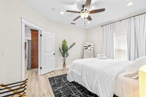 A bedroom with a bed, a ceiling fan, a potted plant, and a window with curtains. - Barefoot Bungalow For 4 (Tampa)
