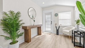 Una sala de estar moderna con piso de madera, chimenea blanca, un espejo grande y una planta en maceta.