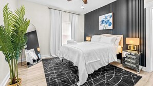 Un dormitorio moderno con cama, lámparas de noche, ventilador de techo, un espejo grande y una planta en maceta.