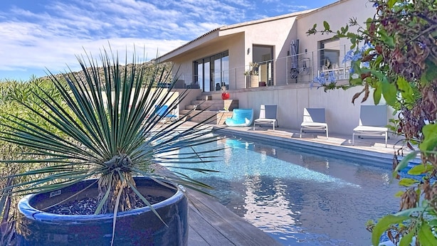 Une maison moderne dotée d’une piscine, d’un espace salon extérieur et d’un escalier menant à un balcon.