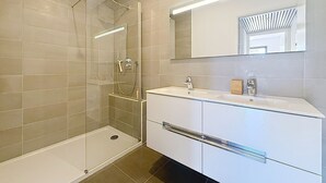Une salle de bain moderne avec une douche à parois de verre, un meuble-lavabo blanc avec un miroir et des murs recouverts de carreaux beiges.