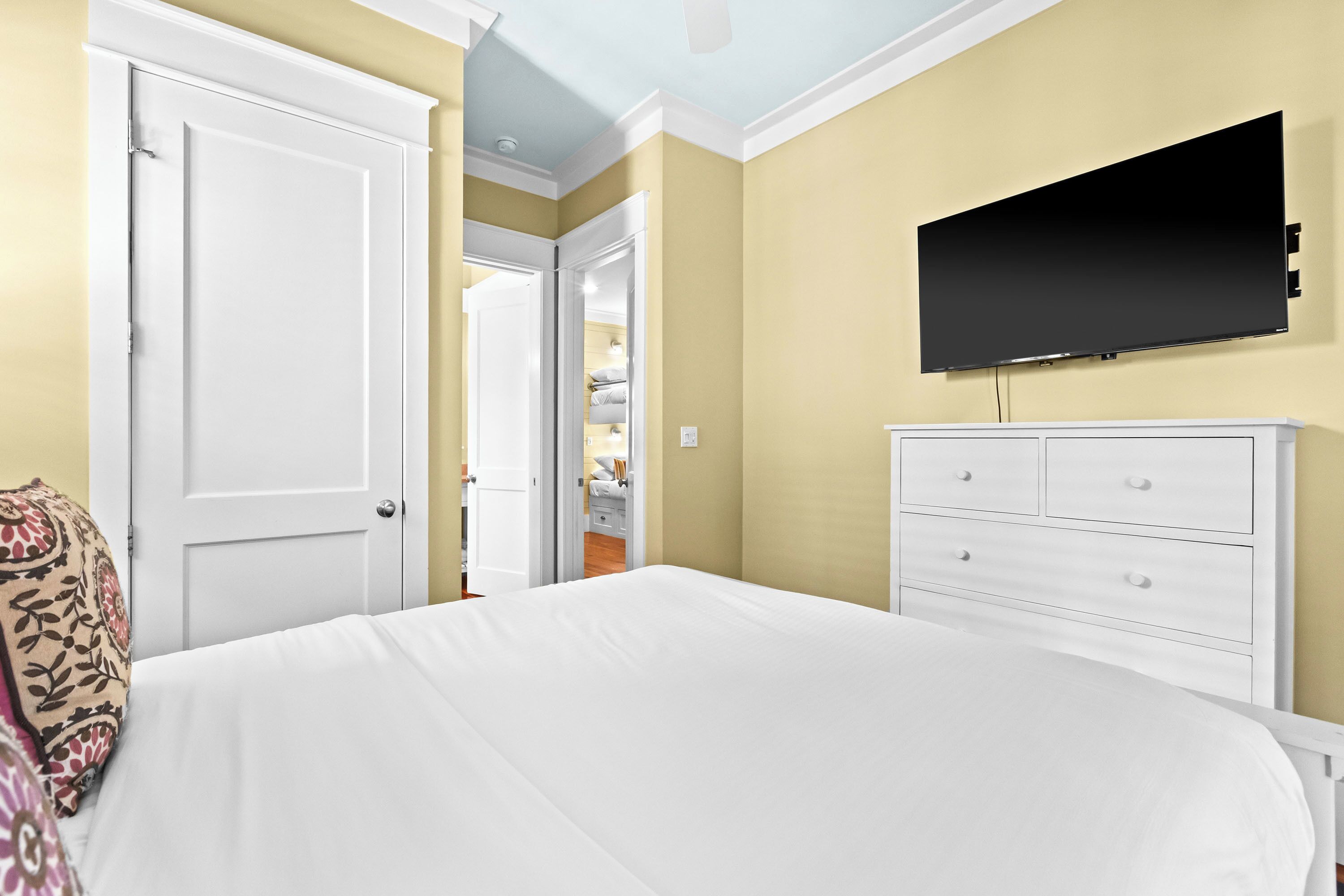 A bedroom with a bed, a dresser, and a television on the wall.