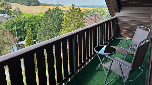 Ein Balkon mit Blick auf eine grüne Landschaft, ein Stuhl und ein kleiner Tisch.