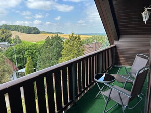 A balcony with a view of a green landscape, a chair, and a small table.