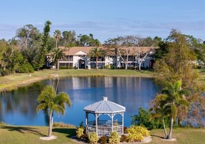 A gazebo near a pond with a building in the background.