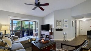A spacious living room with a large window, a ceiling fan, a flat-screen TV, and a fireplace. - Delightful 2-bedroom condo with AC in Fort Myers (Fort Myers)