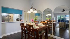 A dining area with a wooden table and chairs, a blue accent wall, and a kitchen in the background. - Delightful 2-bedroom condo with AC in Fort Myers (Fort Myers)