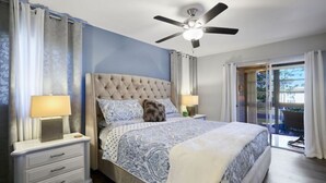 A bedroom with a tufted headboard, a large bed with patterned bedding, two bedside lamps, a nightstand, and a view of the outdoors through a sliding glass door. - Delightful 2-bedroom condo with AC in Fort Myers (Fort Myers)