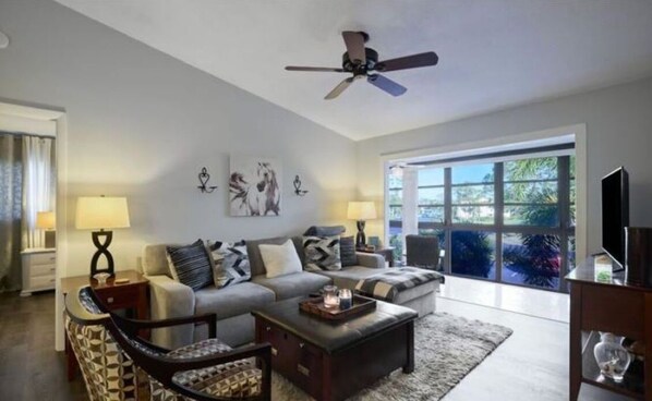 A spacious living room with a large window, a ceiling fan, and a sofa set.