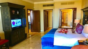 A hotel room with a bed, a television, a ceiling fan, and a door leading to another room.