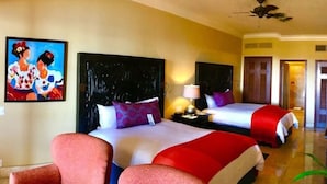 A hotel room with two beds, a ceiling fan, and a painting on the wall.