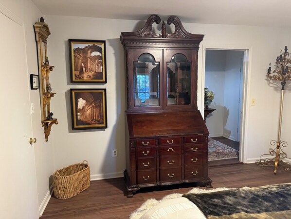 Una habitación con un mueble de madera oscura con puertas de cristal, una cesta de mimbre y cuadros en la pared.