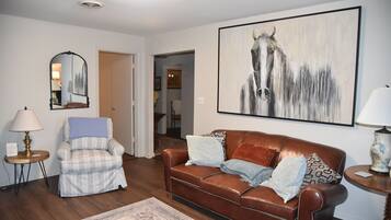 Una sala de estar con un sofá de cuero marrón, un sillón a cuadros, un tapete, una pintura de caballos y un espejo.