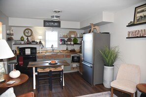 A kitchen with a refrigerator, sink, and wooden countertops. There is a dining table with chairs and a potted plant.