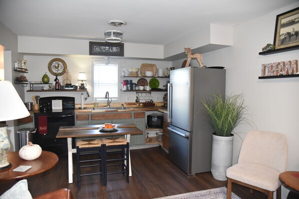Una cocina con refrigerador, lavamanos y encimeras de madera. Se ve una mesa de comedor con sillas y una planta en maceta.
