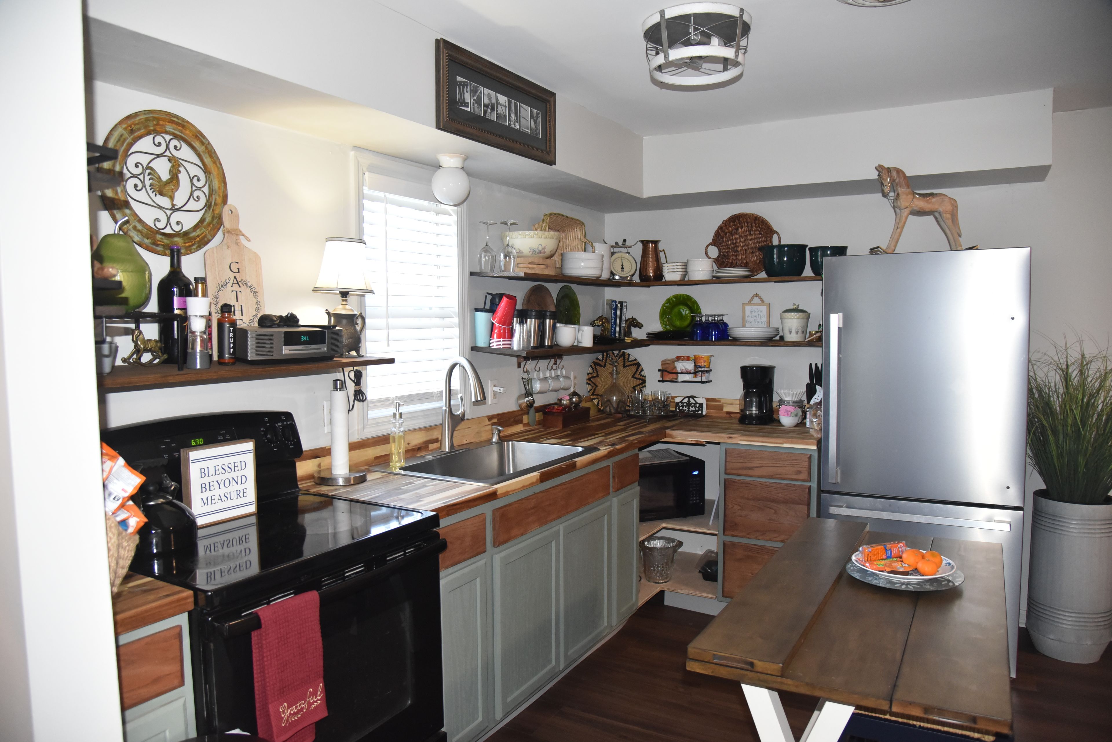 A kitchen with a stainless steel refrigerator, wooden cabinets, a sink, and various kitchen items on shelves.