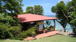 A small, single-story building with a red roof, surrounded by lush greenery and a view of the sea. - Studio with sea view, beach, air conditioning, bar-restaurant, swimming pool, car rental (Sainte-Anne)