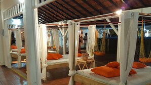 A series of wooden beds with white canopies and orange pillows, arranged in a row under a high ceiling with exposed beams. - Studio with sea view, beach, air conditioning, bar-restaurant, swimming pool, car rental (Sainte-Anne)