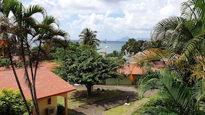 A tropical resort with palm trees, a red-roofed building, and a view of the sea. - Studio with sea view, beach, air conditioning, bar-restaurant, swimming pool, car rental (Sainte-Anne)