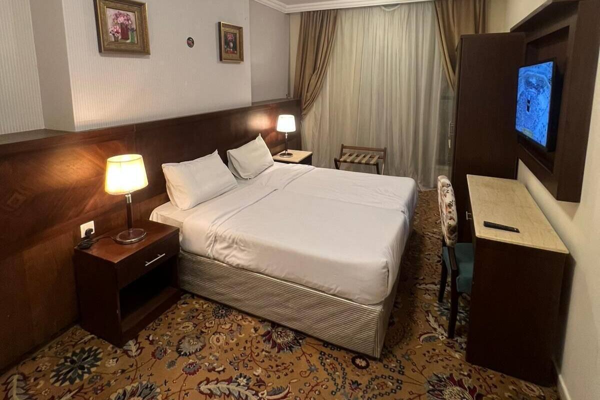 Ein Hotelzimmer mit einem großen Bett, zwei Nachttischen mit Lampen, einem Fernseher und einem gemusterten Teppich.