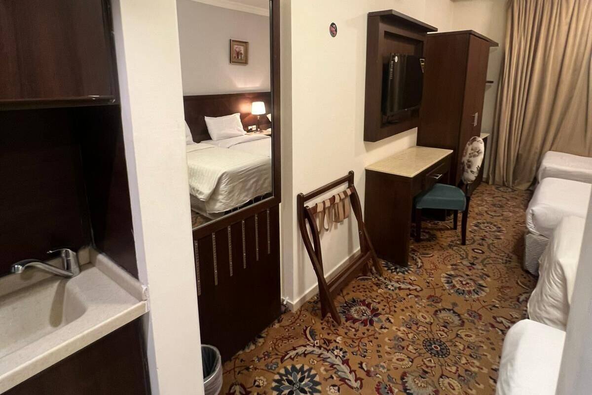 Ein Hotelzimmer mit einem Bett, einem Schreibtisch, einem Fernseher, einem Sessel, einem kleinen Tisch, einem Waschbecken und Teppichboden.