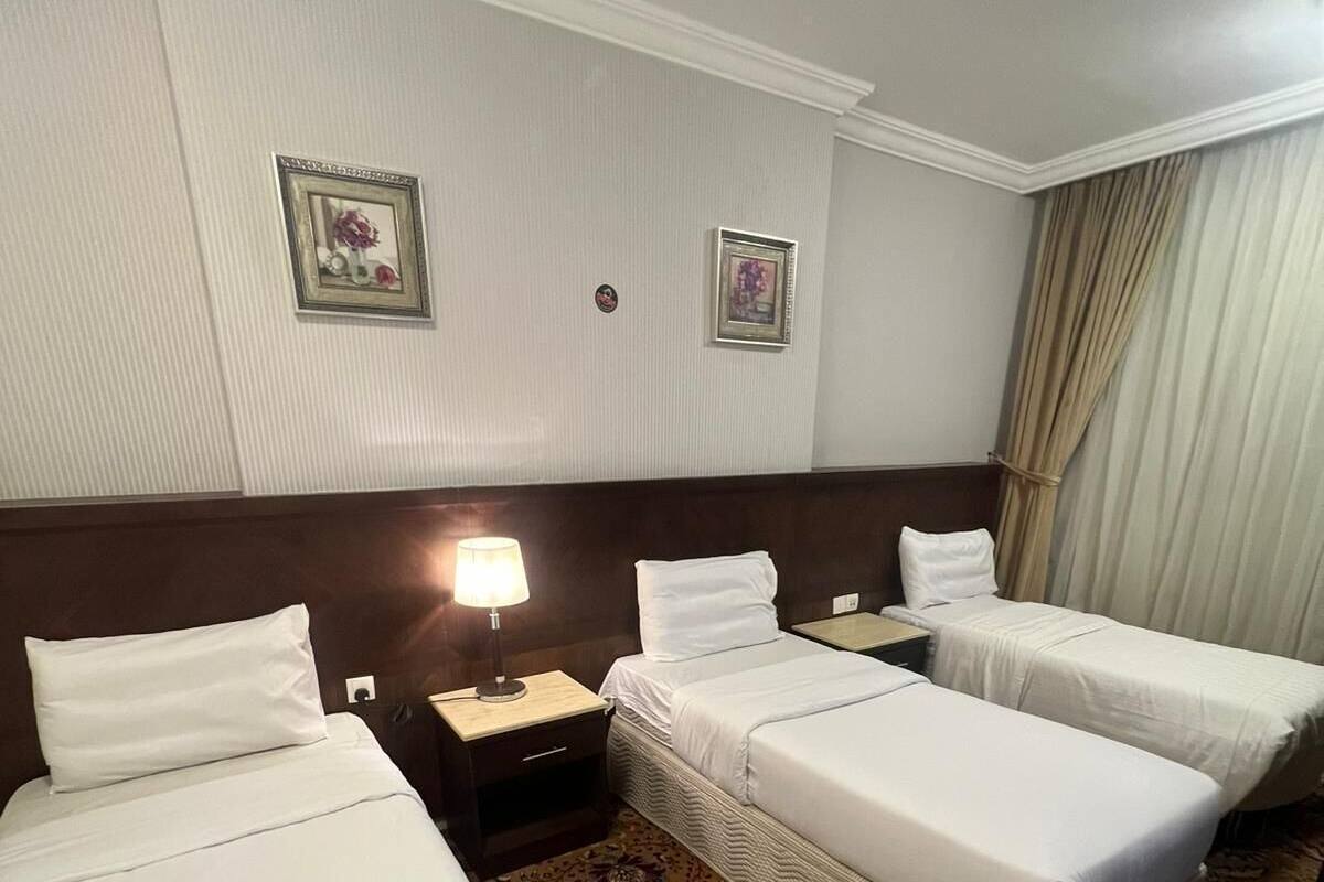 Ein Hotelzimmer mit drei Einzelbetten, einem Nachttisch mit Lampe und einem gemusterten Teppich.