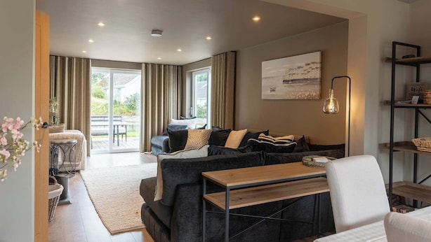 A modern living room with a sofa, a wooden coffee table, and a dining area with a bench. - 4 Bed Holiday Home by Guestz (Rhosneigr)