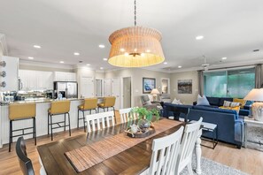 Una cocina moderna con armarios blancos, un comedor con mesa de madera y una sala de estar con sofá azul.