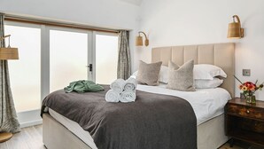Un dormitorio bien iluminado con una cama grande, una mesita de noche con un jarrón de flores y vistas al exterior a través de una puerta corrediza.