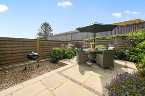Une terrasse extérieure avec une table ronde et des chaises en osier, un barbecue et une clôture en bois.