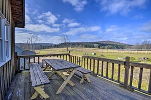 Une terrasse en bois avec des tables de pique-nique, donnant sur un champ verdoyant et des collines.