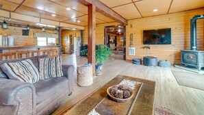 A cozy cabin interior with a wooden ceiling, a sofa, a coffee table with pinecones, a television, and a wood-burning stove. - Lakeside Gem: Hot Tub & Game Room in Hancock (Hancock)