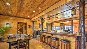 A wooden interior with a bar area, stools, and a dining table set for four. - Lakeside Gem: Hot Tub & Game Room in Hancock (Hancock)