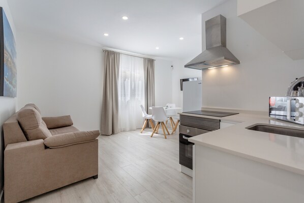 Una cocina moderna con horno empotrado, un comedor con mesa y sillas blancas, y un sofá beige.