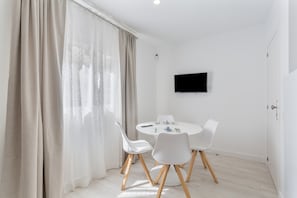 A modern dining area with a round table, white chairs, and a flat-screen TV mounted on the wall.