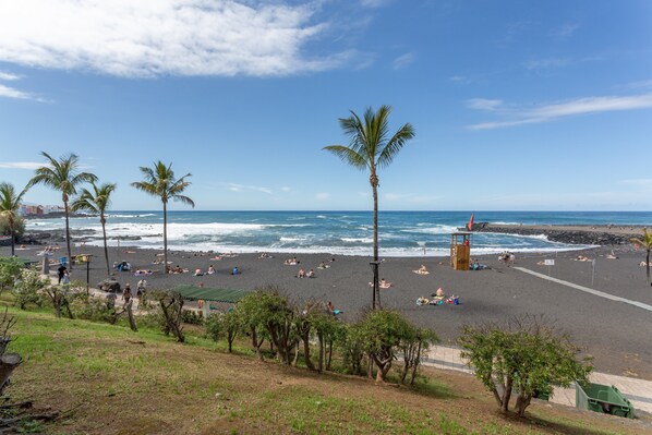 A beach with palm trees, a lifeguard tower, and a rocky shoreline.