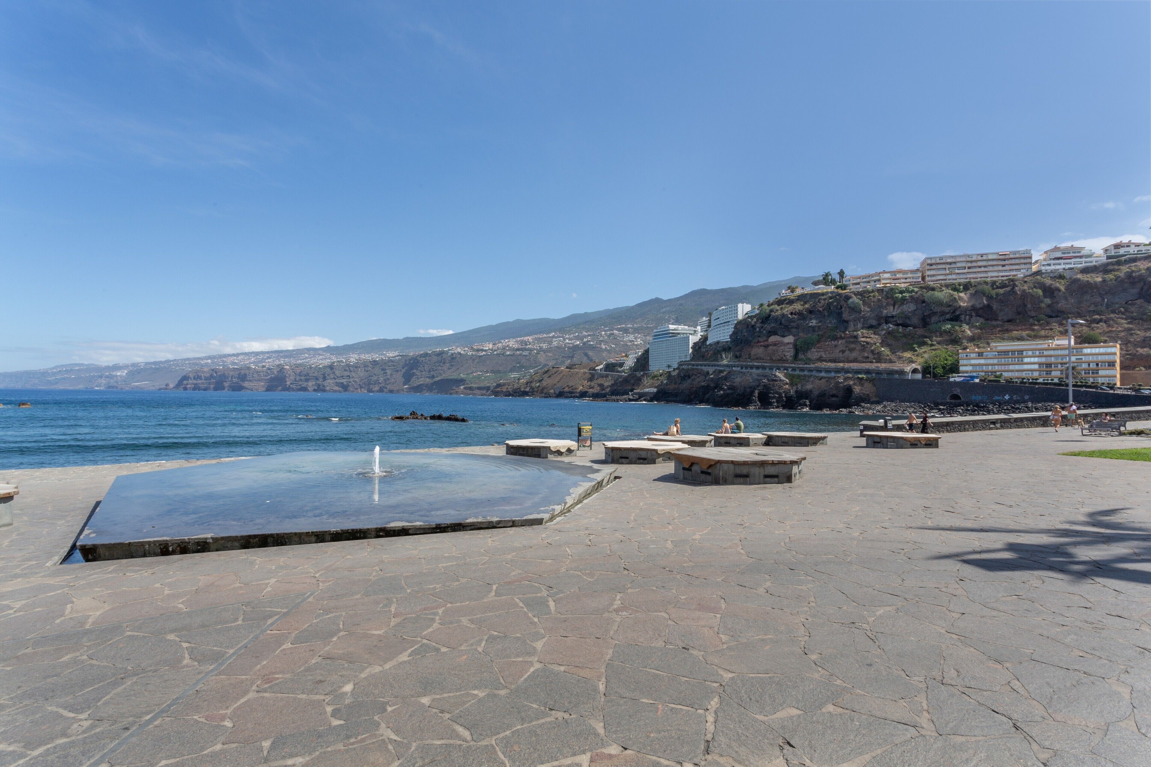 Une promenade en bord de mer avec un sol en pierre, une piscine et des bâtiments en arrière-plan.