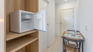 A compact room with a white refrigerator, a wooden cabinet, a dining table with chairs, and a door leading to another room.
