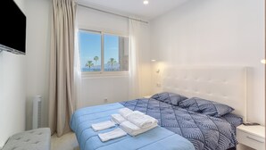 A bedroom with a bed, a bedside table, a TV, and a window with curtains.